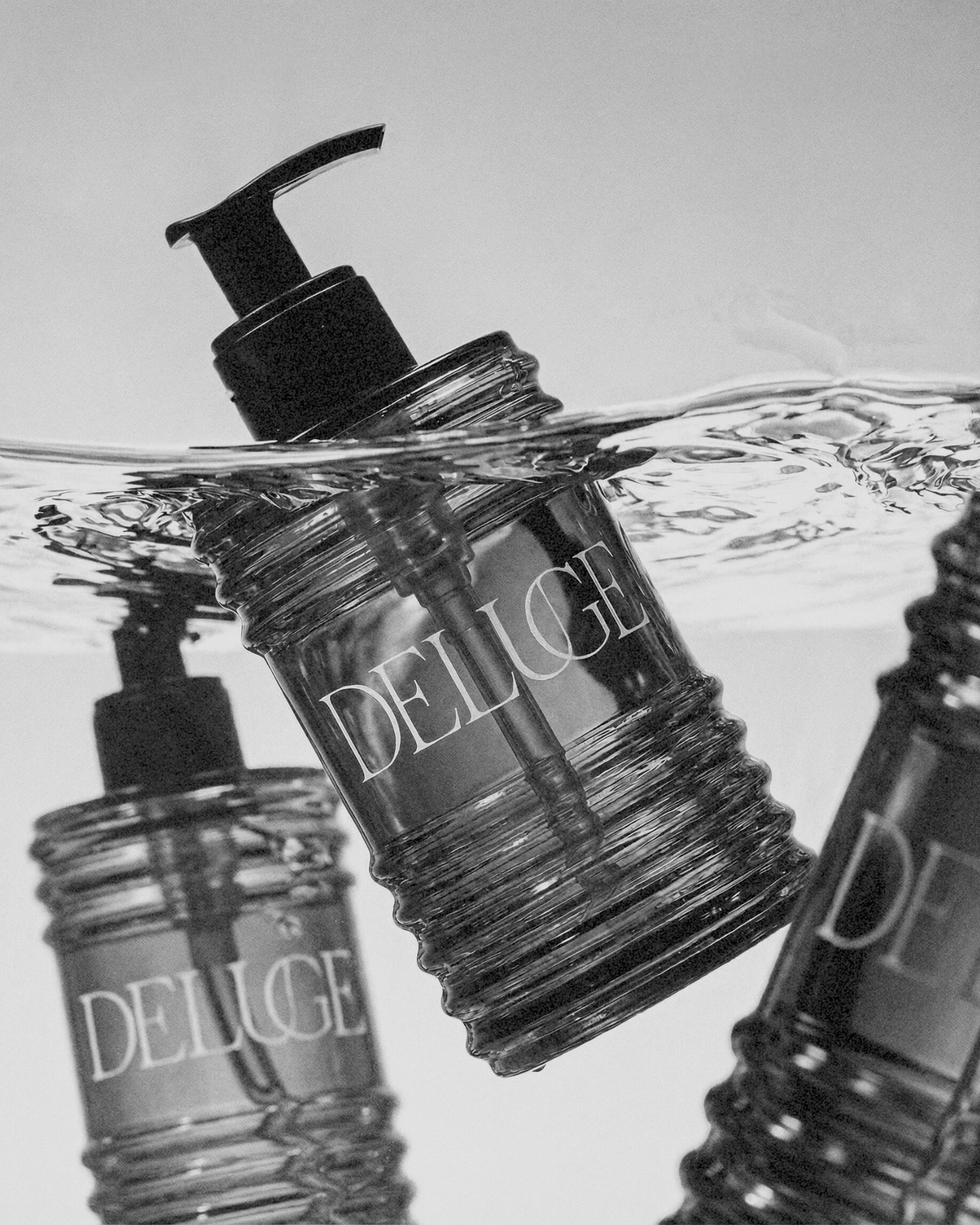 Clear bottles with black pump caps labeled 'Deluge' on a light gray background